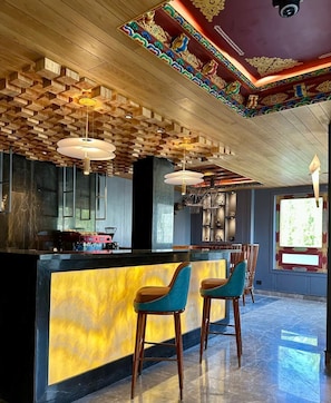 A bar area with a wooden ceiling, bar stools, and a counter with a yellow backlit display. - The Indus Valley (Leh)