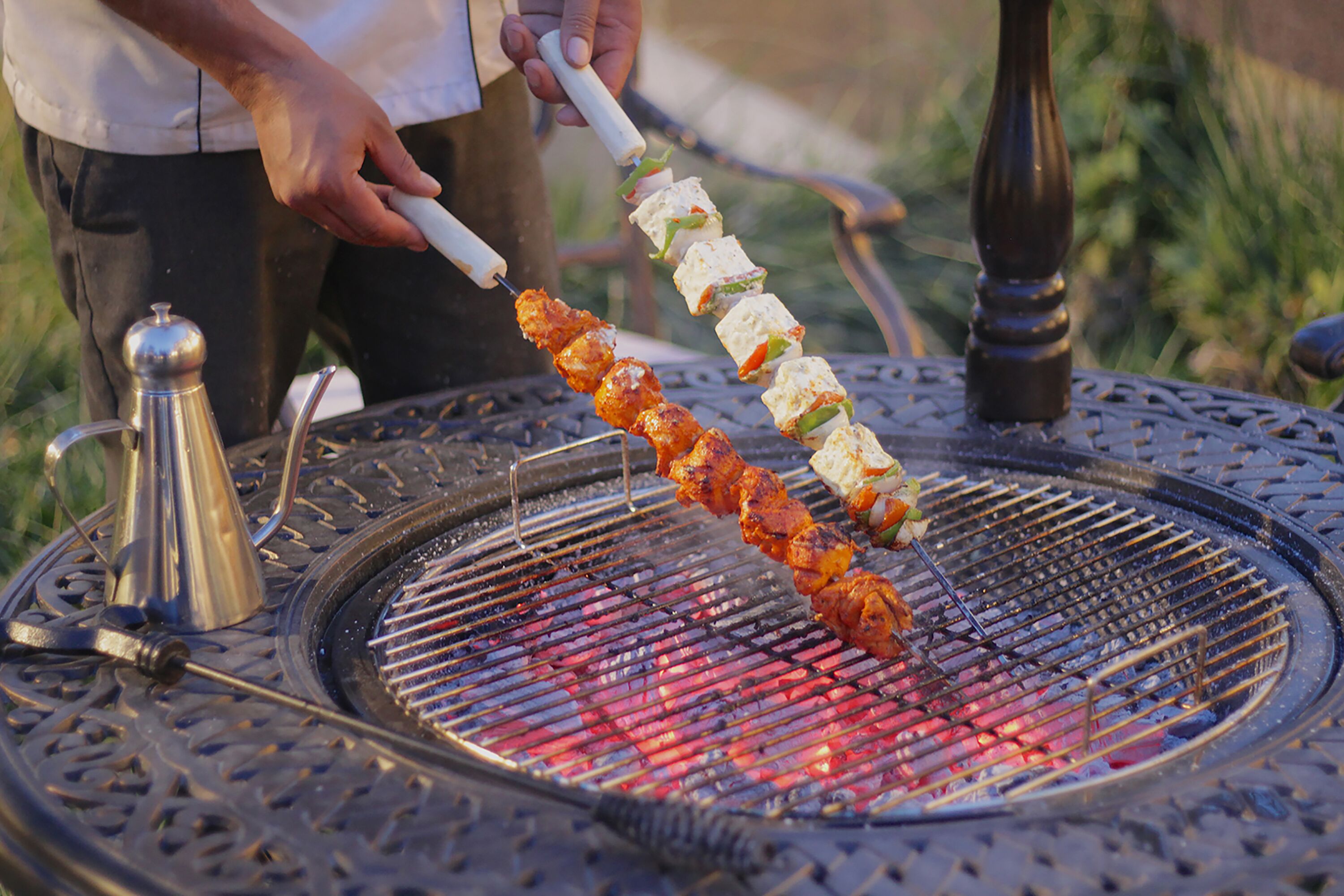 Una persona asando brochetas de carne y vegetales en una parrilla al aire libre.