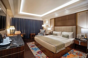 Habitación de hotel con una cama grande, un escritorio con una silla, una mesita pequeña y una lámpara.