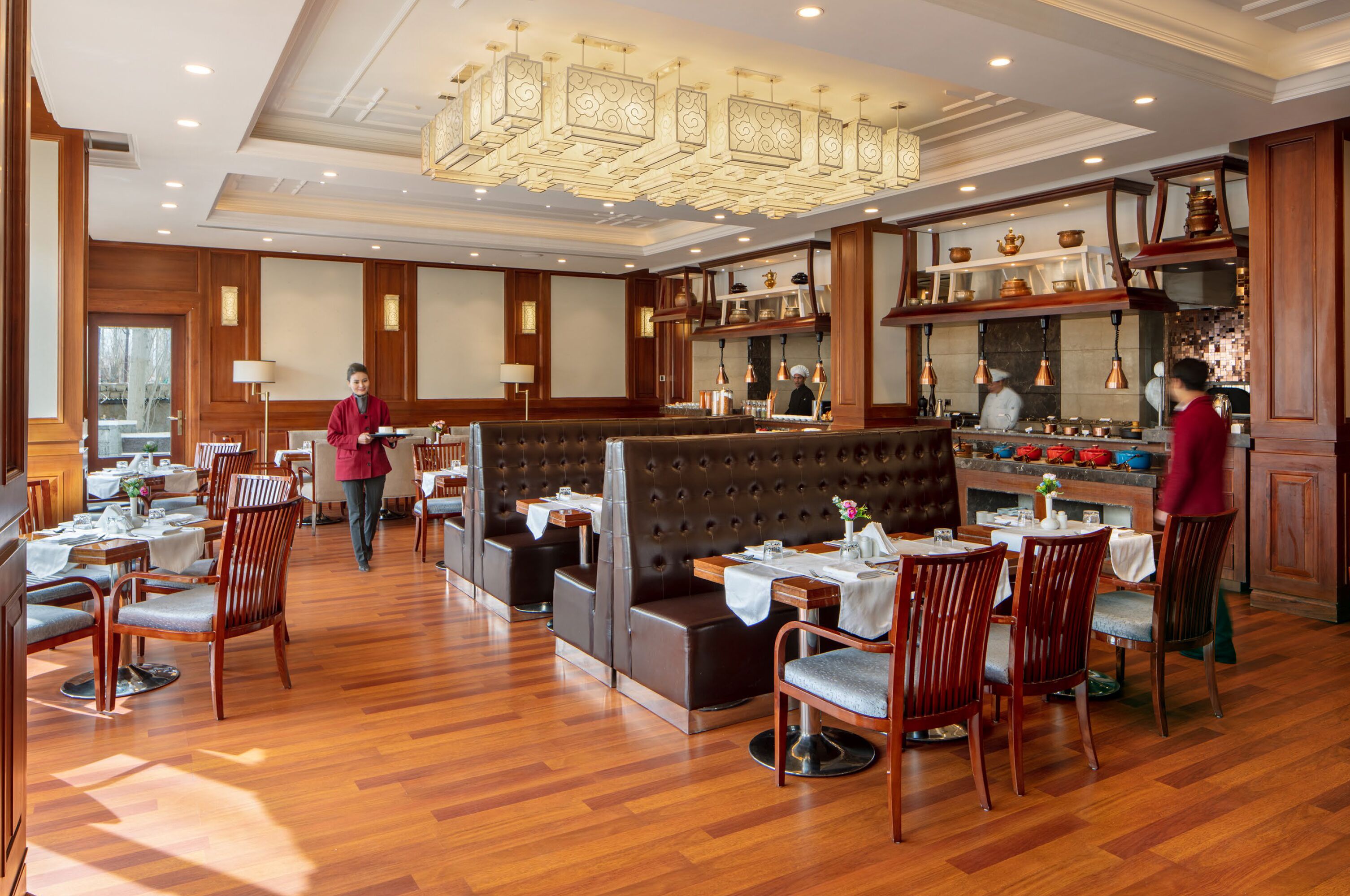 A restaurant with wooden flooring, cushioned seating, and a chef at work.