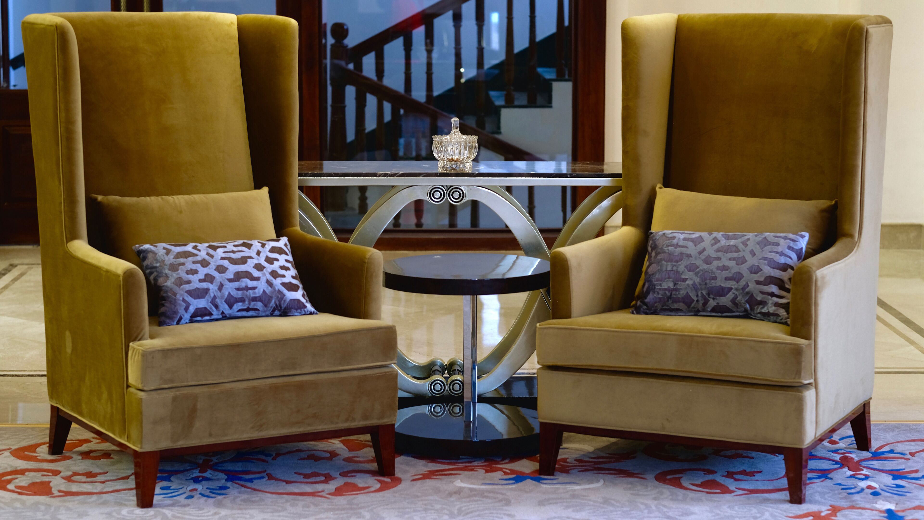 Two armchairs with patterned cushions, a small round table with a decorative item, and a patterned carpet.