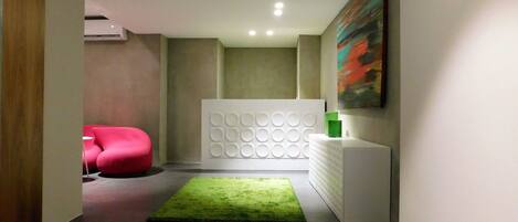 A modern hallway with a green rug, a red chair, a white wall unit with circular patterns, and a painting.