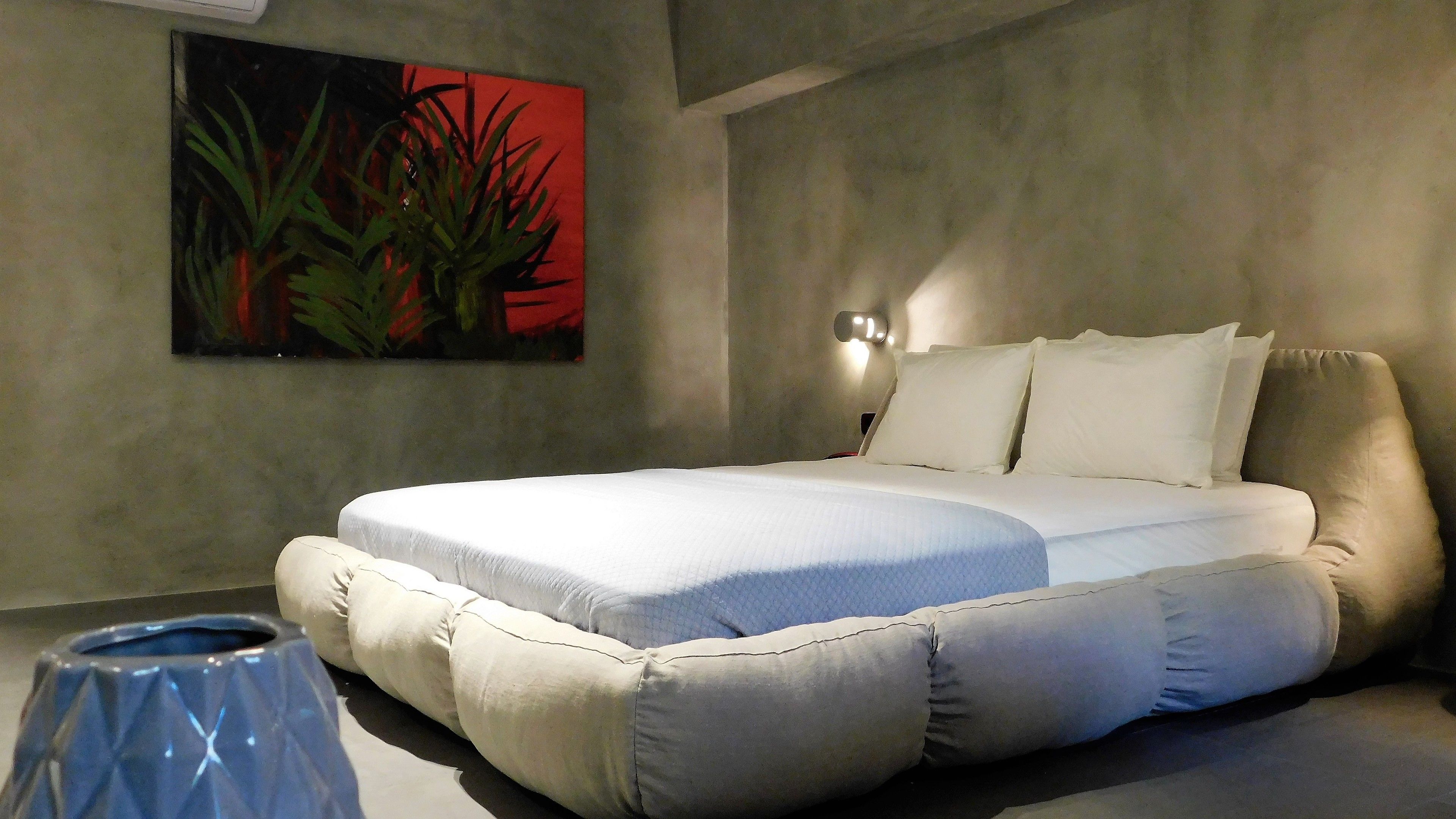 A modern bedroom with a bed, a wall-mounted light, and a painting.