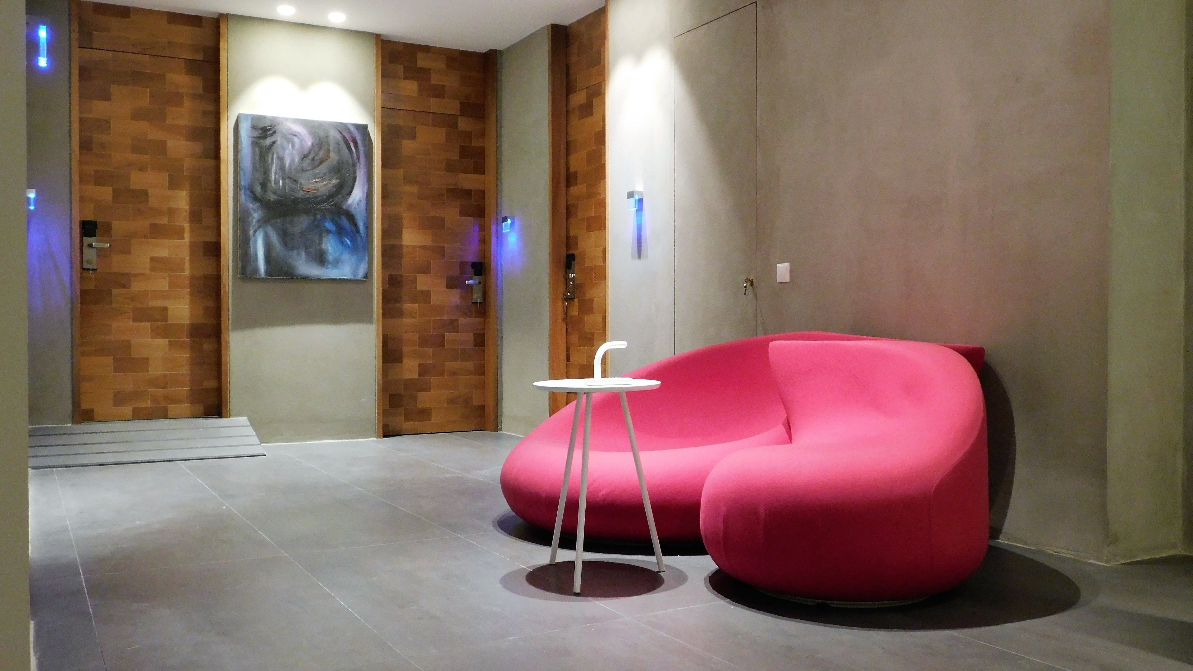 A modern lobby with a red sofa, a small white table, and a large abstract painting on the wall.