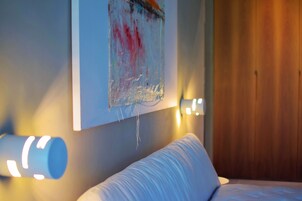 Un dormitorio con cama, una obra de arte en la pared y una lámpara de noche.