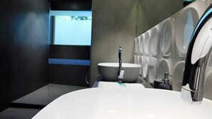 A modern bathroom with a large white sink, a mirror, and a wall-mounted toilet.