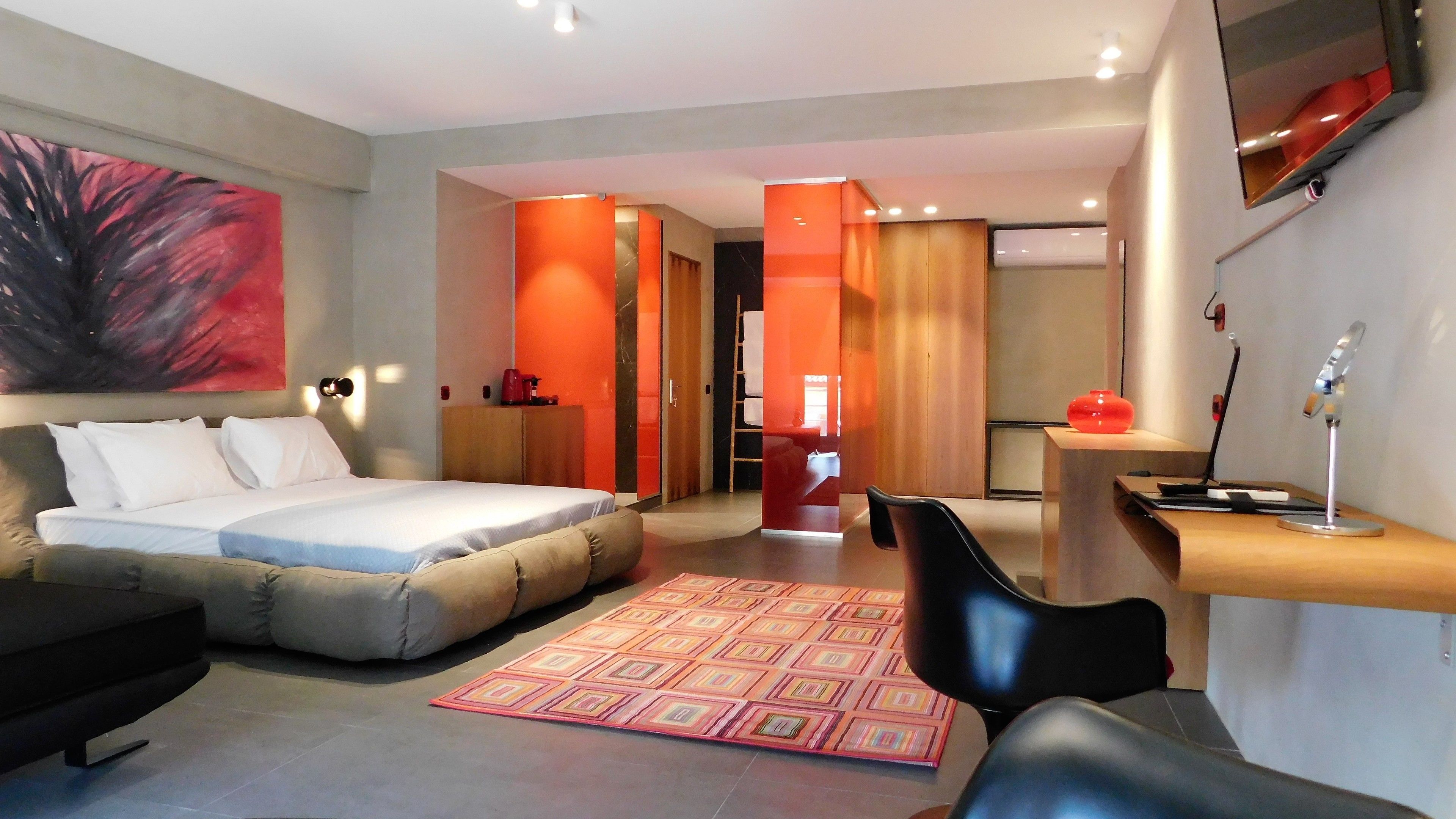 A modern hotel room with a large bed, a desk, a chair, and a TV.