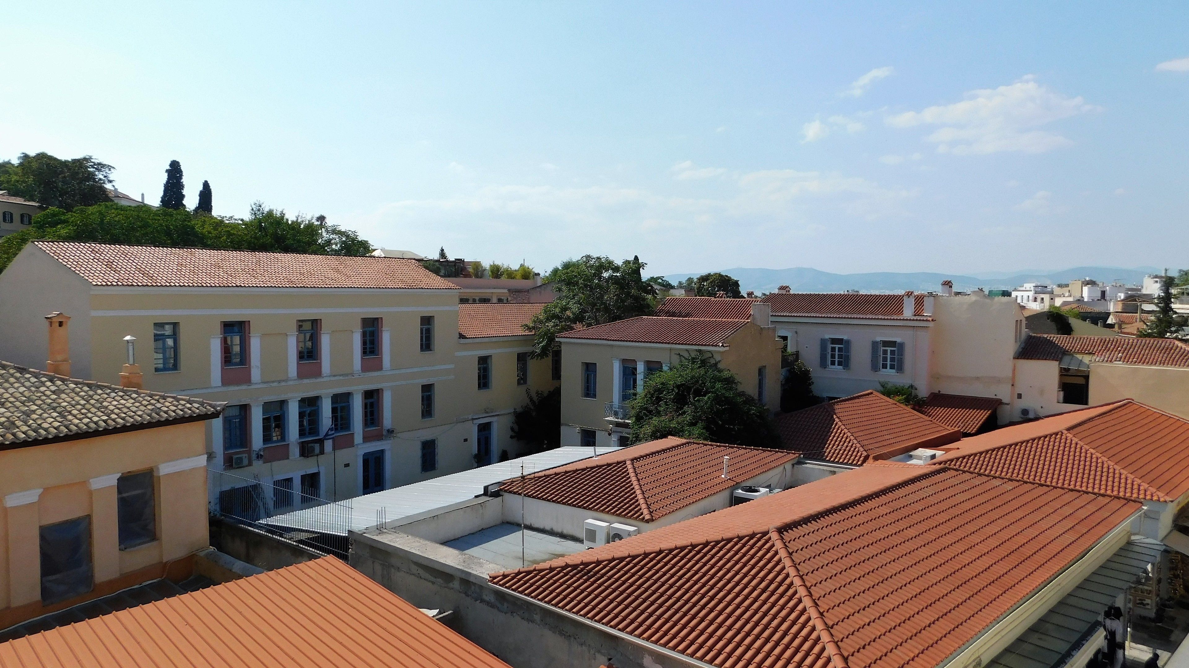 A residential area with terracotta-tiled roofs, multi-story buildings, and a clear sky.