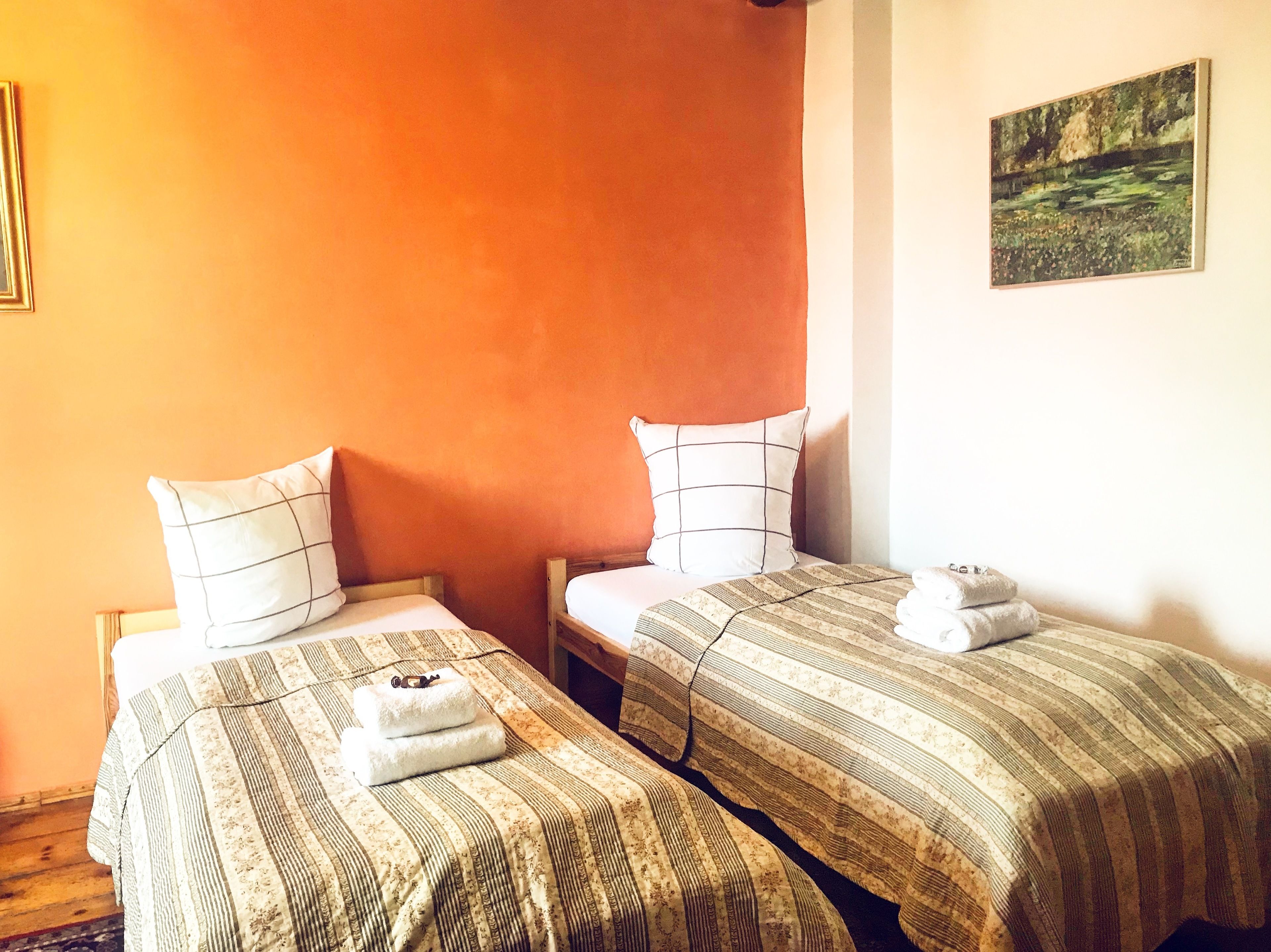 Dos camas individuales con ropa de cama a rayas y almohadas, un cuadro en la pared y suelo de madera.