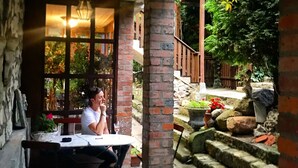 Un patio al aire libre con una columna de ladrillo, una mesa con sillas y una persona sentada.