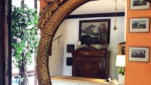 Una habitación con un espejo grande y ornamentado, un aparador de madera, un cuadro y una planta en maceta.