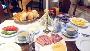 Una mesa de desayuno con diversos alimentos, entre ellos pan, jamón, queso y salchichas, además de bebidas y condimentos.