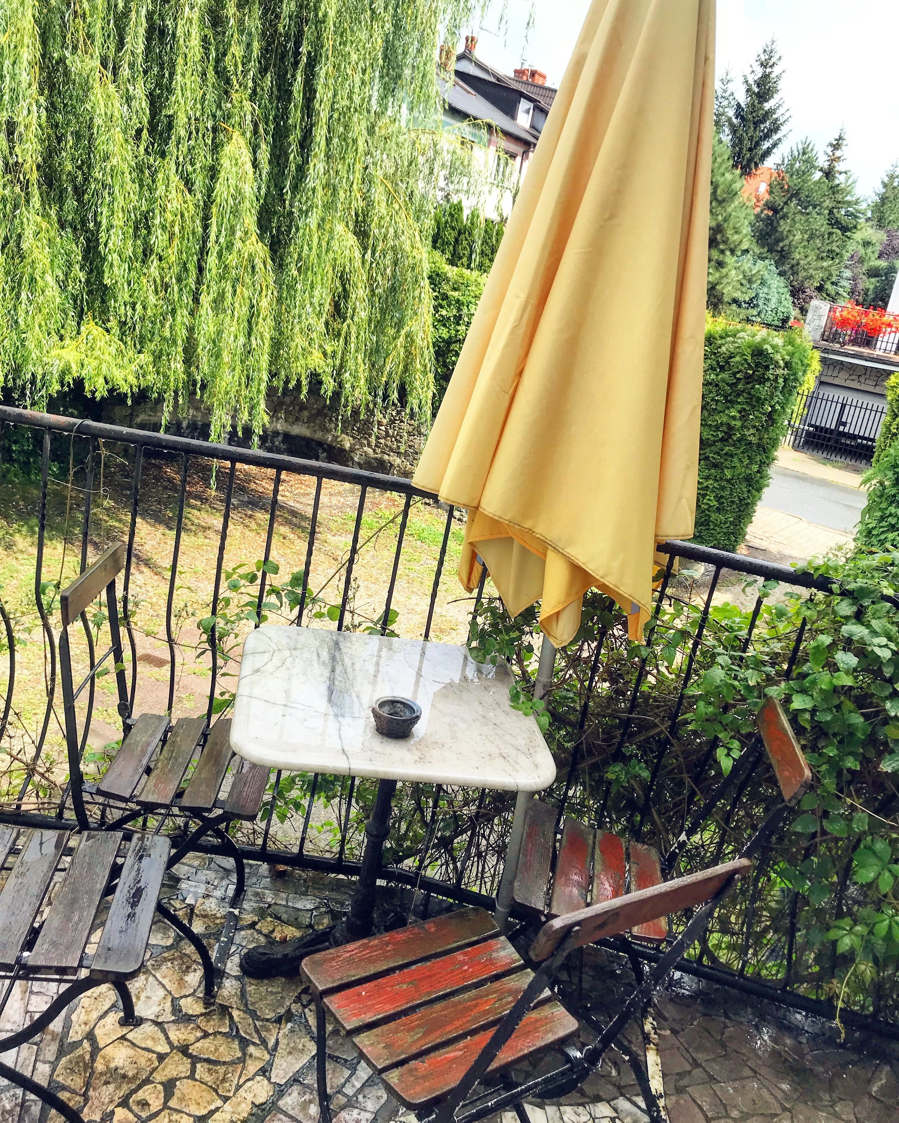 Una pequeña zona de estar al aire libre con una mesa y sillas, rodeada por una valla de metal y follaje.