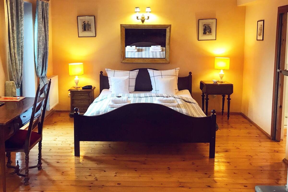 A bedroom with a wooden bed, two bedside tables with lamps, a chair, and a desk.