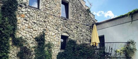 A stone building with multiple windows, some covered by vines, and a yellow umbrella on the balcony.