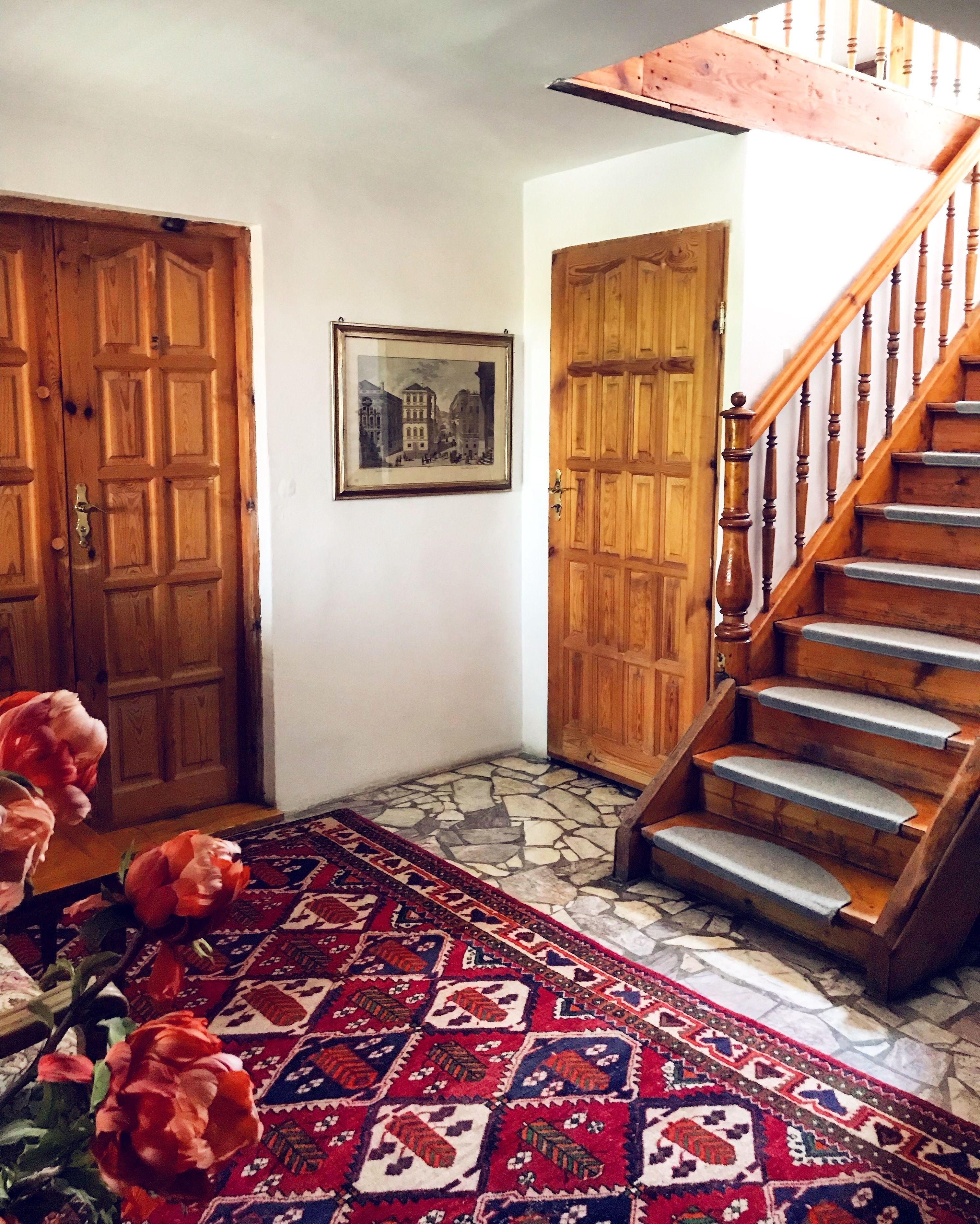 A hallway with wooden doors, a staircase, and a patterned rug.