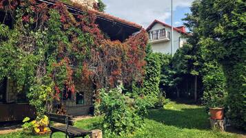 Ein Steingebäude mit Gartenanlage, einer Bank und einem Baum.