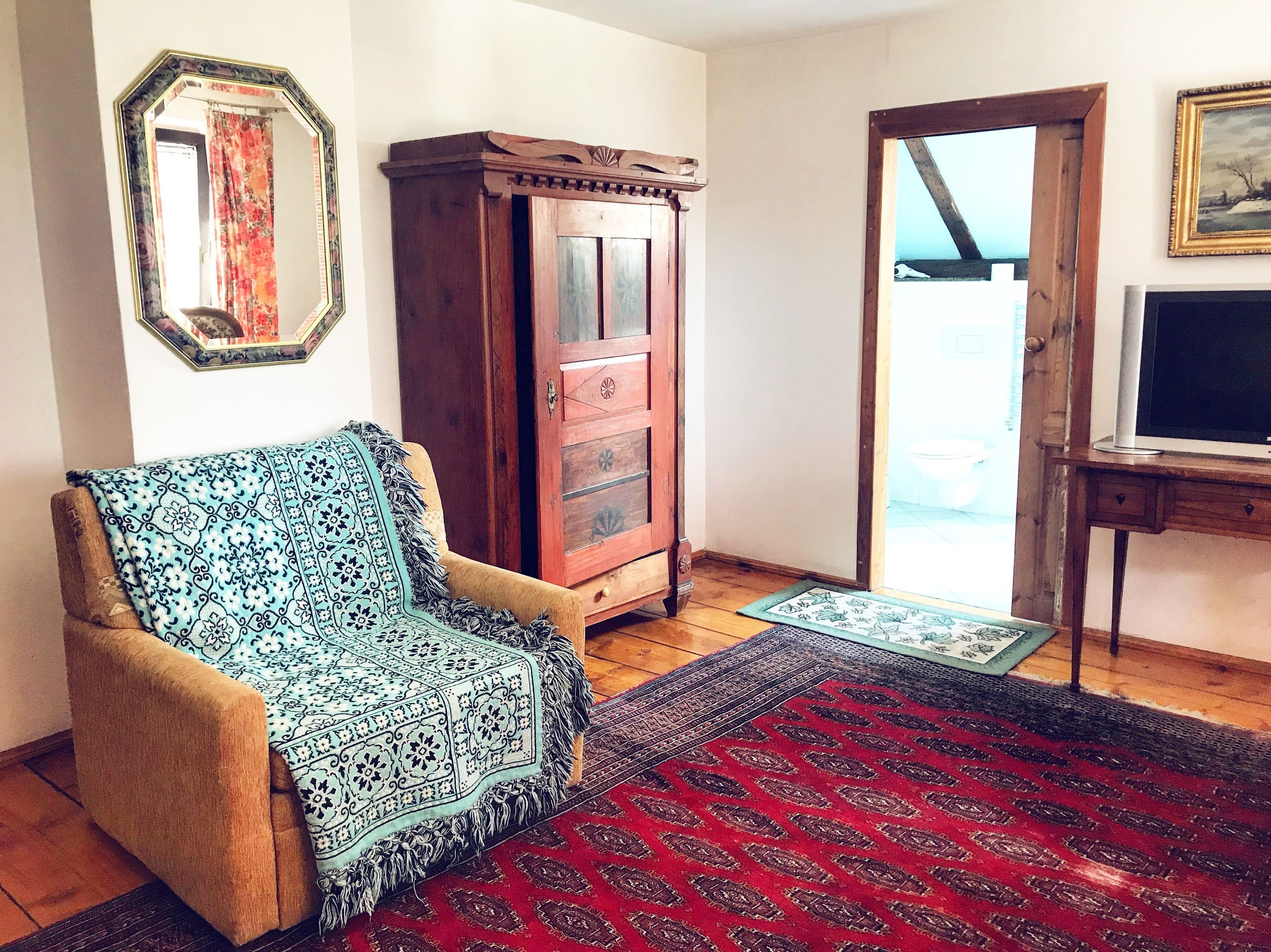 A living room with a wooden cabinet, a patterned armchair, a red and black rug, and a television on a wooden stand.