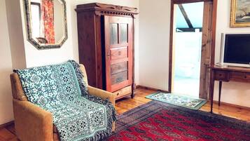 A living room with a wooden cabinet, a patterned armchair, a red and black rug, and a television on a wooden stand.