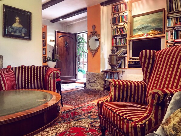 Un salón acogedor con una mesa de centro de madera, sillones a rayas, una estantería y un cuadro grande en la pared.