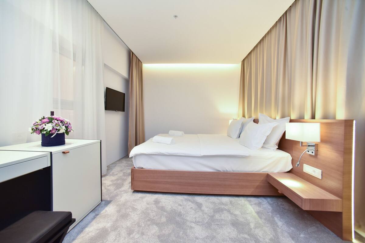 A modern hotel room with a bed, bedside table, desk, and a small plant.