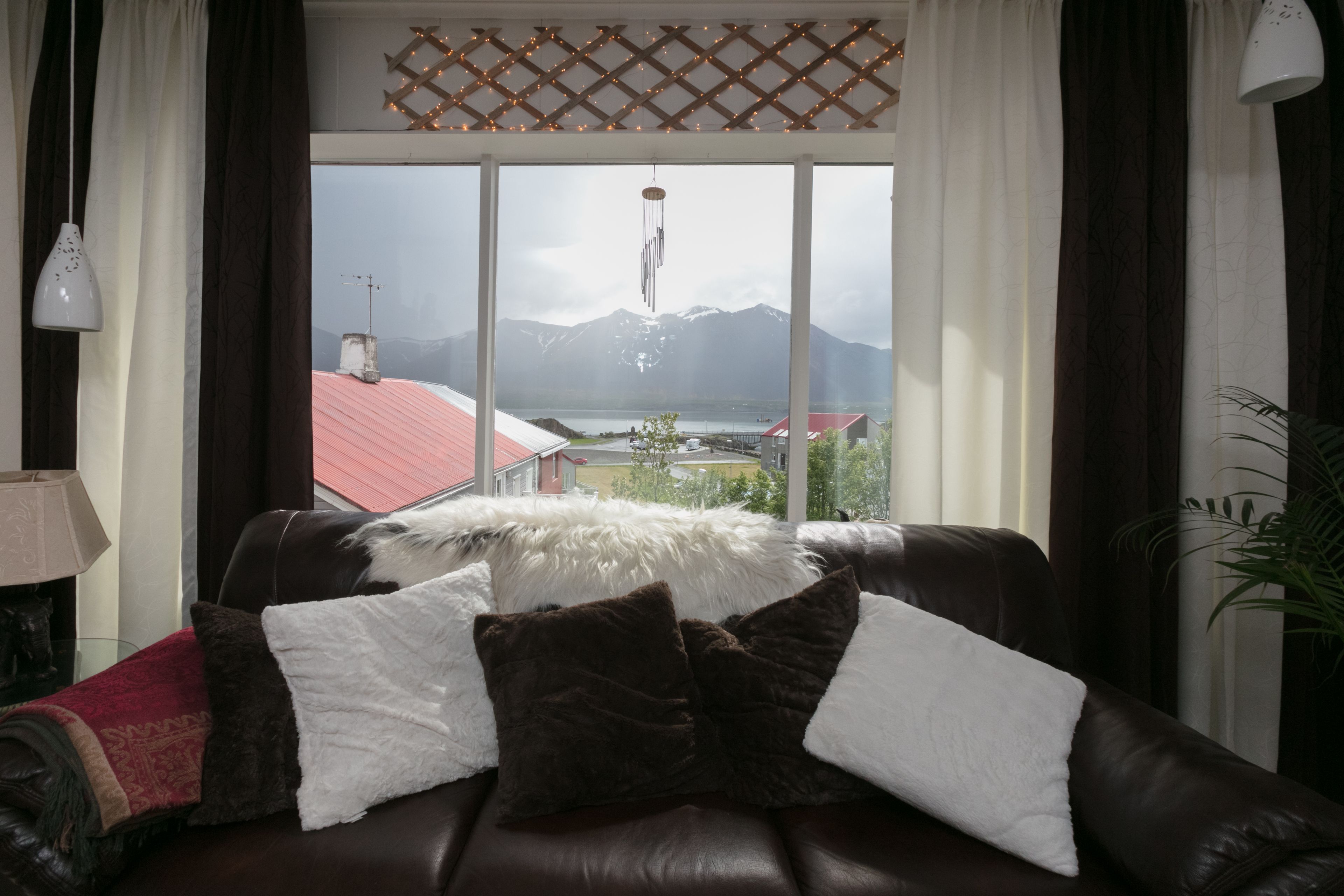 A living room with a leather sofa, a view of mountains, and a red-roofed building through a large window.