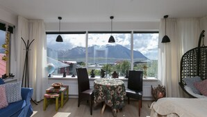 Una habitación con un ventanal grande, una mesa redonda, un sofá azul y una cama con una silla colgante.