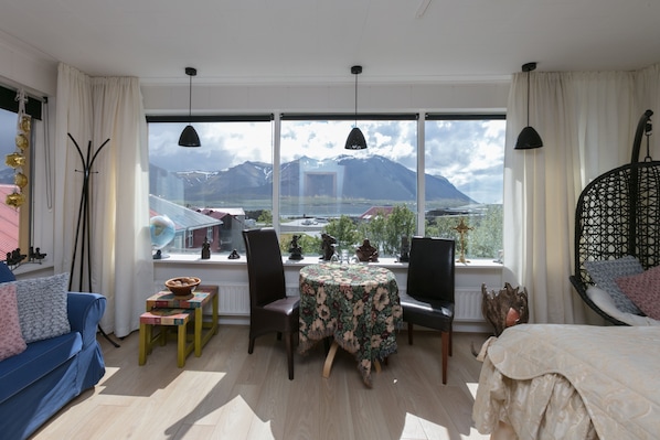Una habitación con un ventanal grande, una mesa redonda, un sofá azul y una cama con una silla colgante.