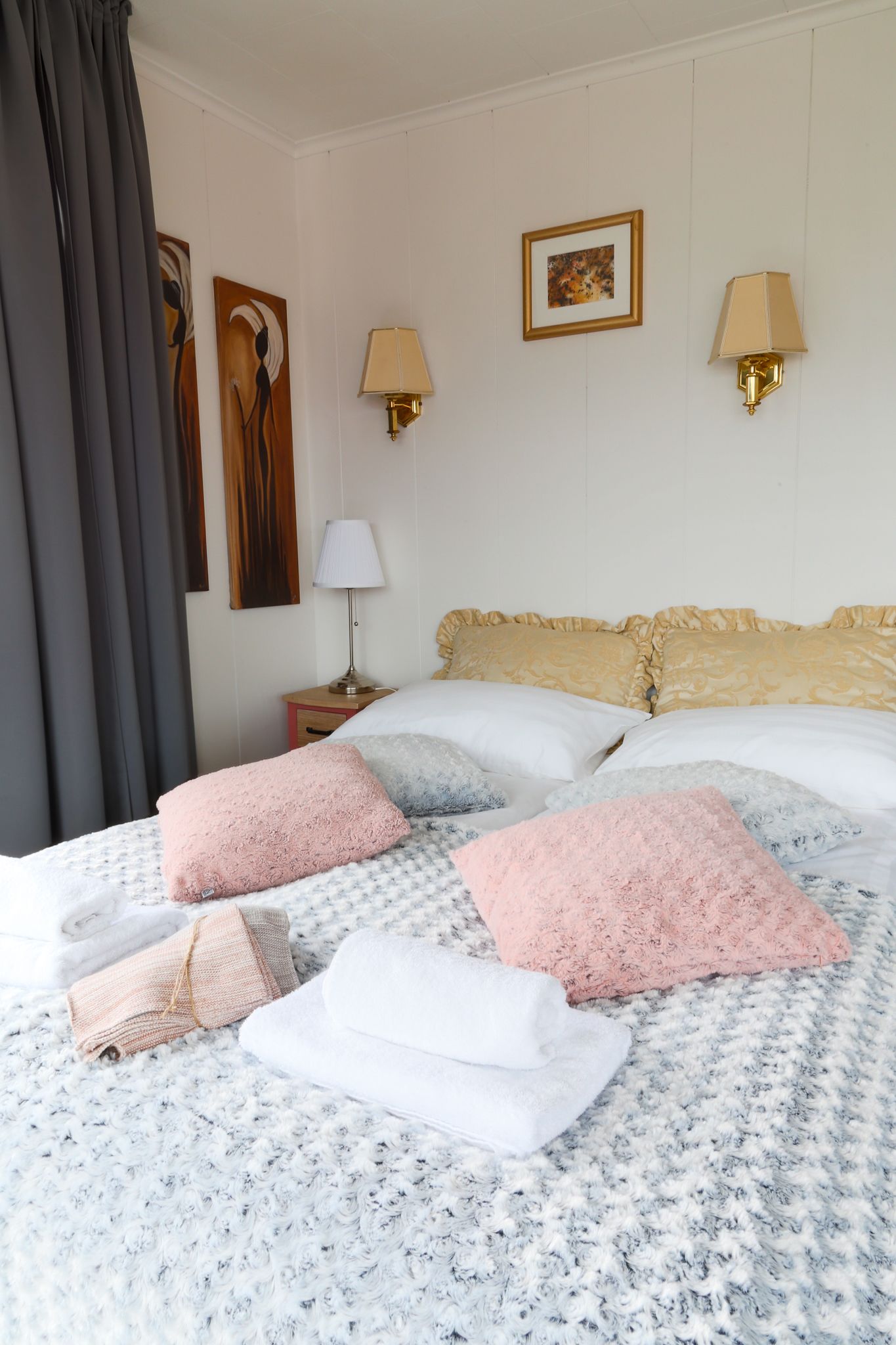 Een netjes opgemaakt bed met beddengoed met patroon, twee wandlampen en een ingelijste foto aan de muur.