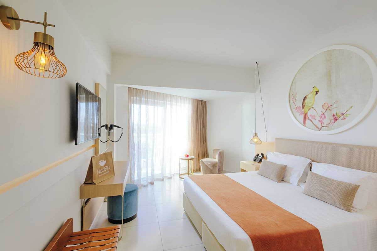 A hotel room with a bed, a desk, a chair, a TV, and a painting on the wall.