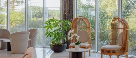 Un interior moderno con ventanas amplias, sillas de mimbre, una mesa redonda de vidrio y una planta en maceta.