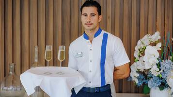 A person in a white shirt with blue stripes holding a table with two glasses of wine.