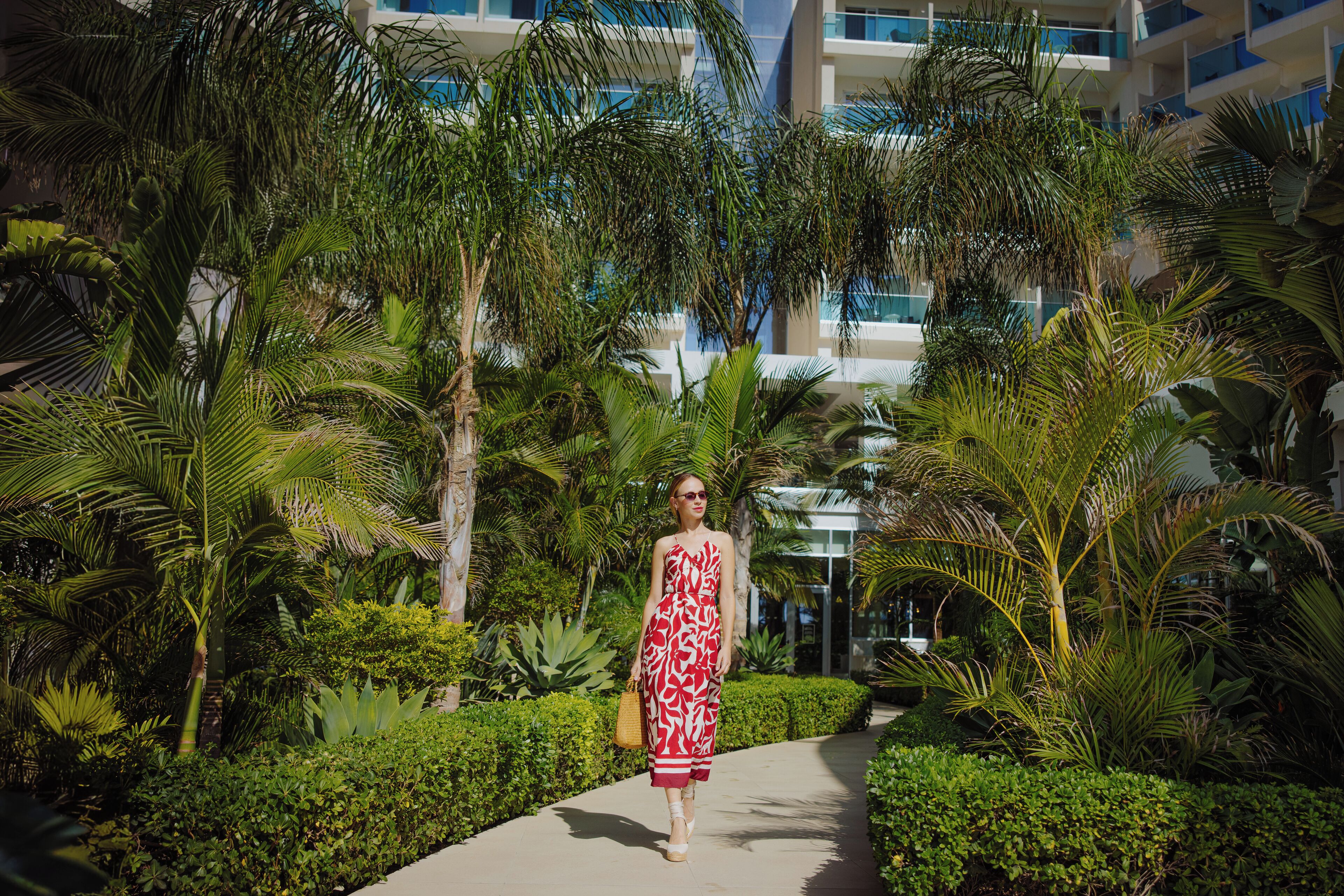 A pathway surrounded by lush greenery and palm trees, leading to a building with multiple balconies.