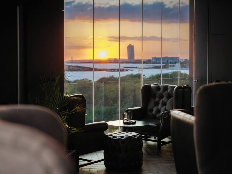 Una sala moderna con vistas a una puesta de sol sobre un cuerpo de agua, que incluye un sofá, un sillón y una mesita.