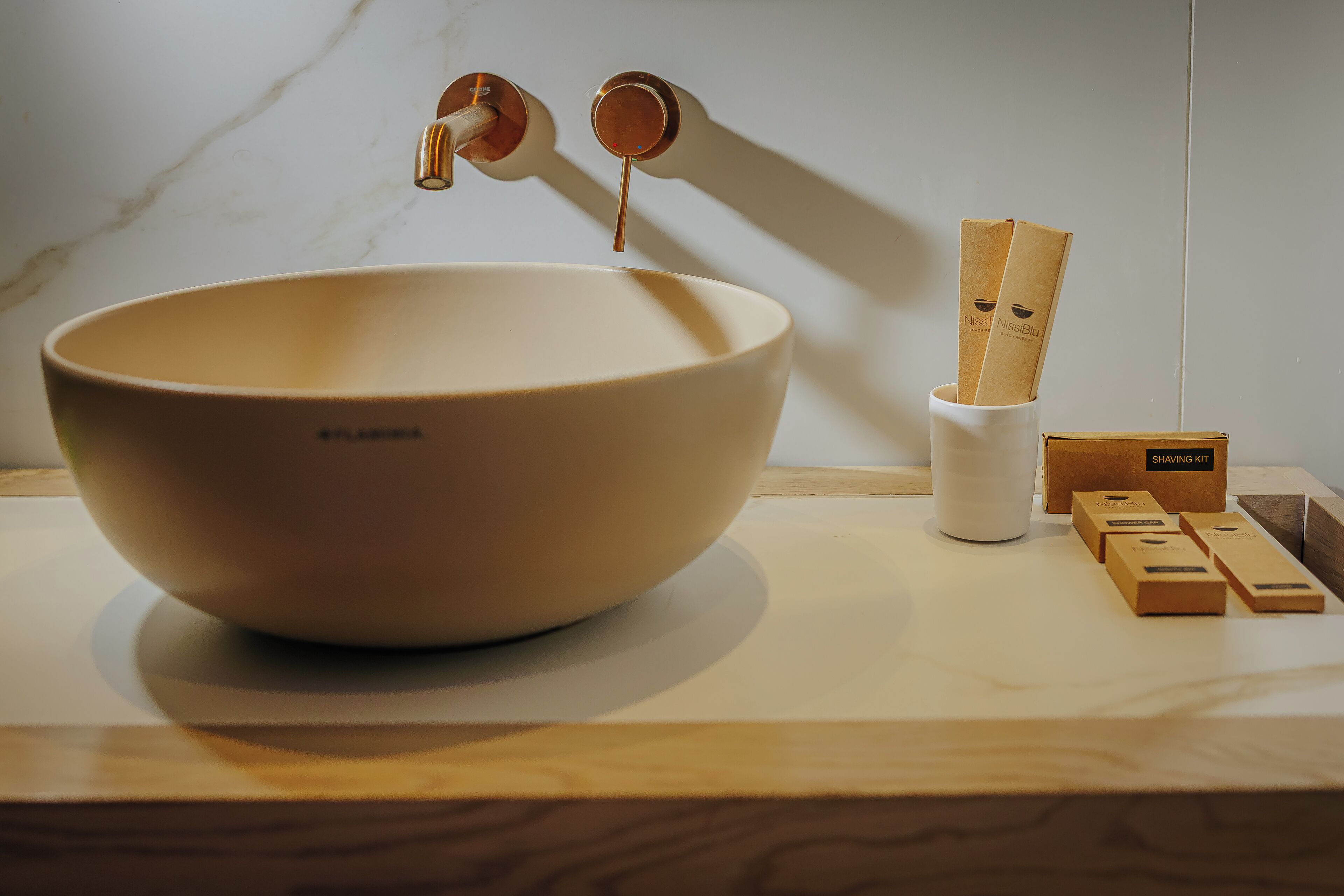 Un grand bol beige posé sur une surface en bois, une tasse blanche et plusieurs boîtes en bois contenant des accessoires de rasage.
