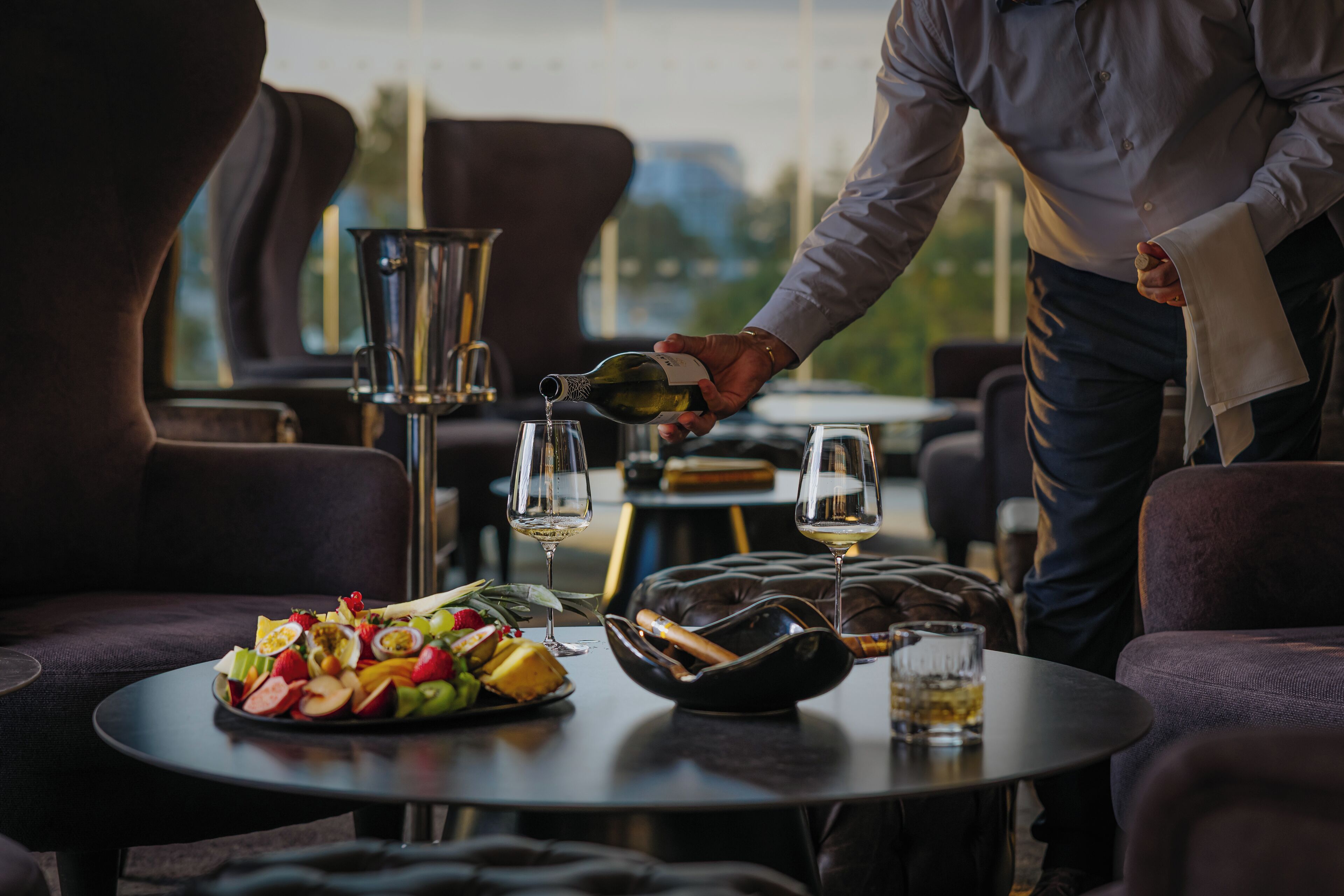 A dining area with a table set for two, featuring a fruit platter, wine glasses, and a bottle of wine.