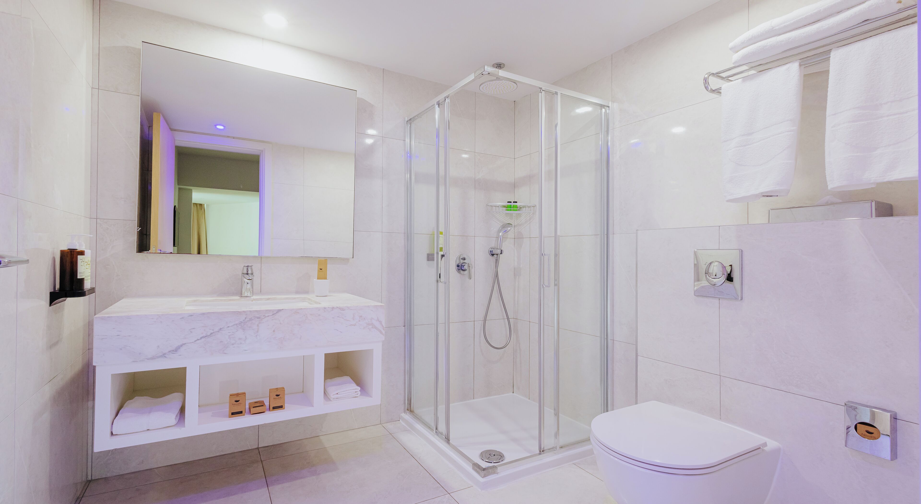 A modern bathroom with a glass-enclosed shower, a white sink with marble countertop, and a toilet.