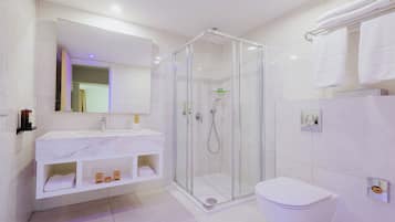 Un baño moderno con ducha de vidrio, un lavamanos blanco y encimera de mármol, y un inodoro.