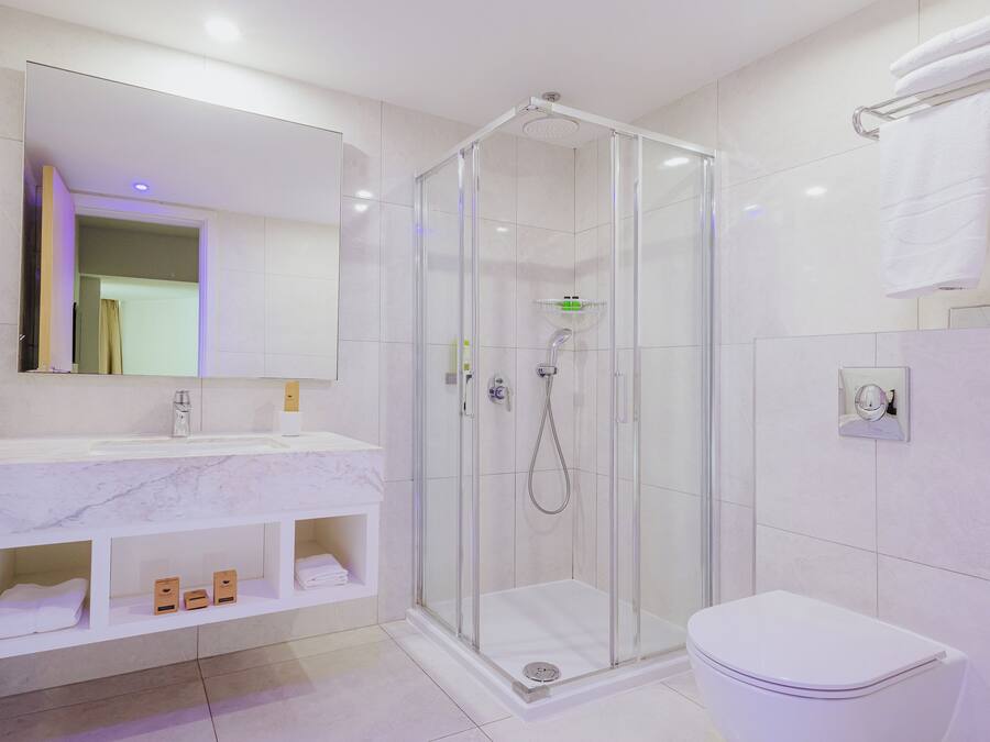 Un baño moderno con ducha de vidrio, un lavamanos blanco y encimera de mármol, y un inodoro.
