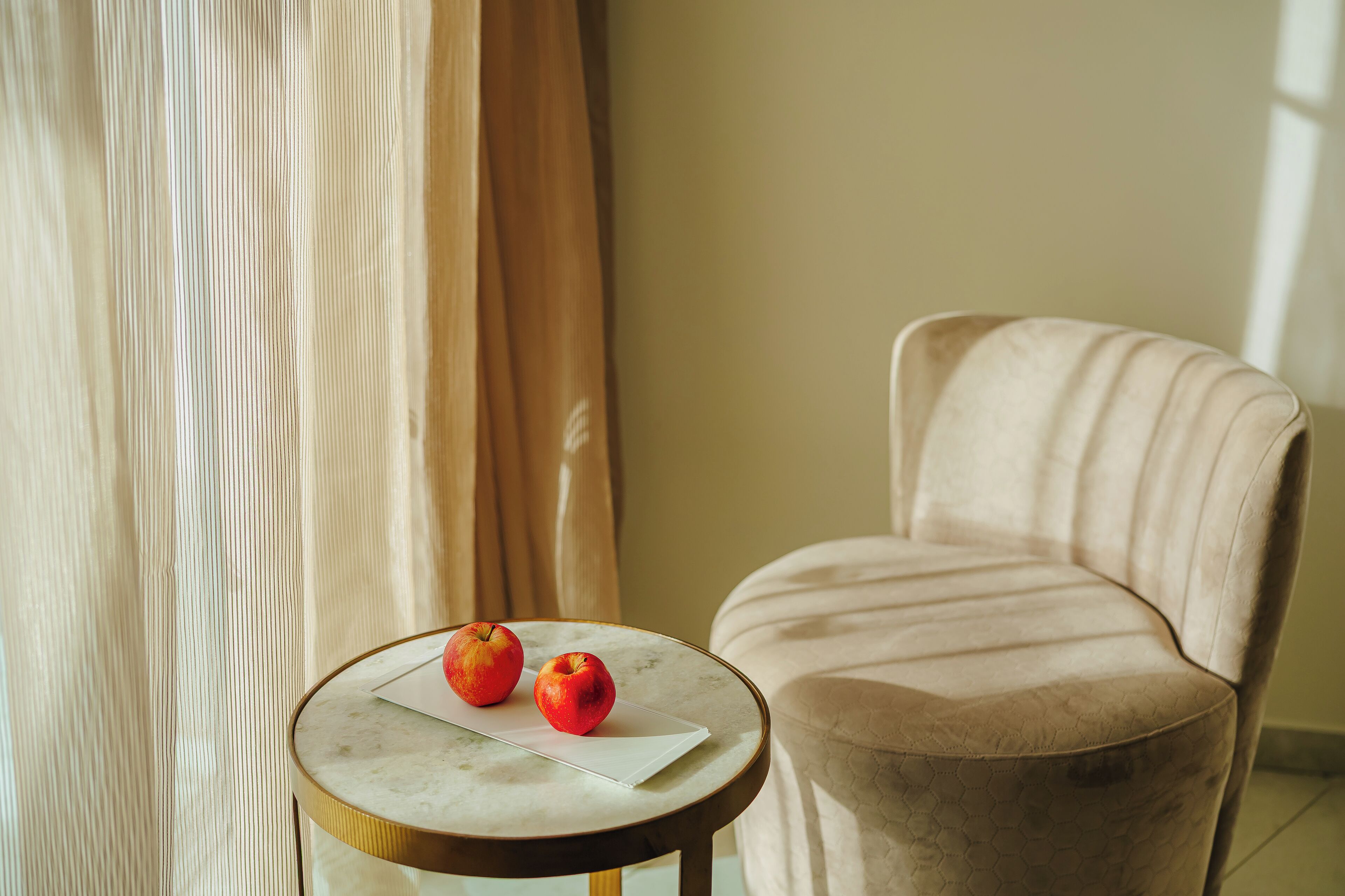 A room with a round table, two apples, a chair, and a curtain.