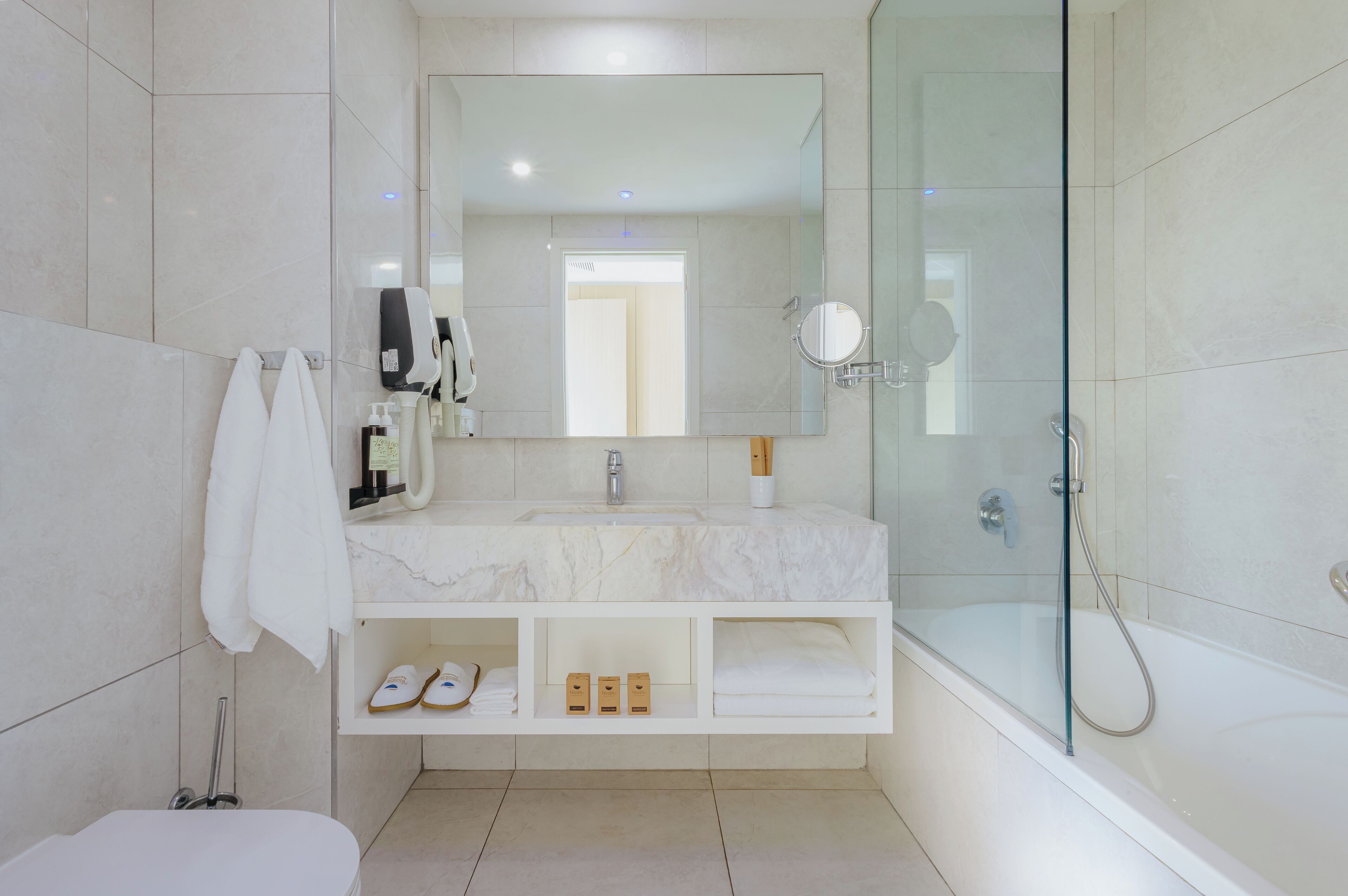 Un baño moderno con ducha de vidrio, un espejo grande y tocador de mármol.