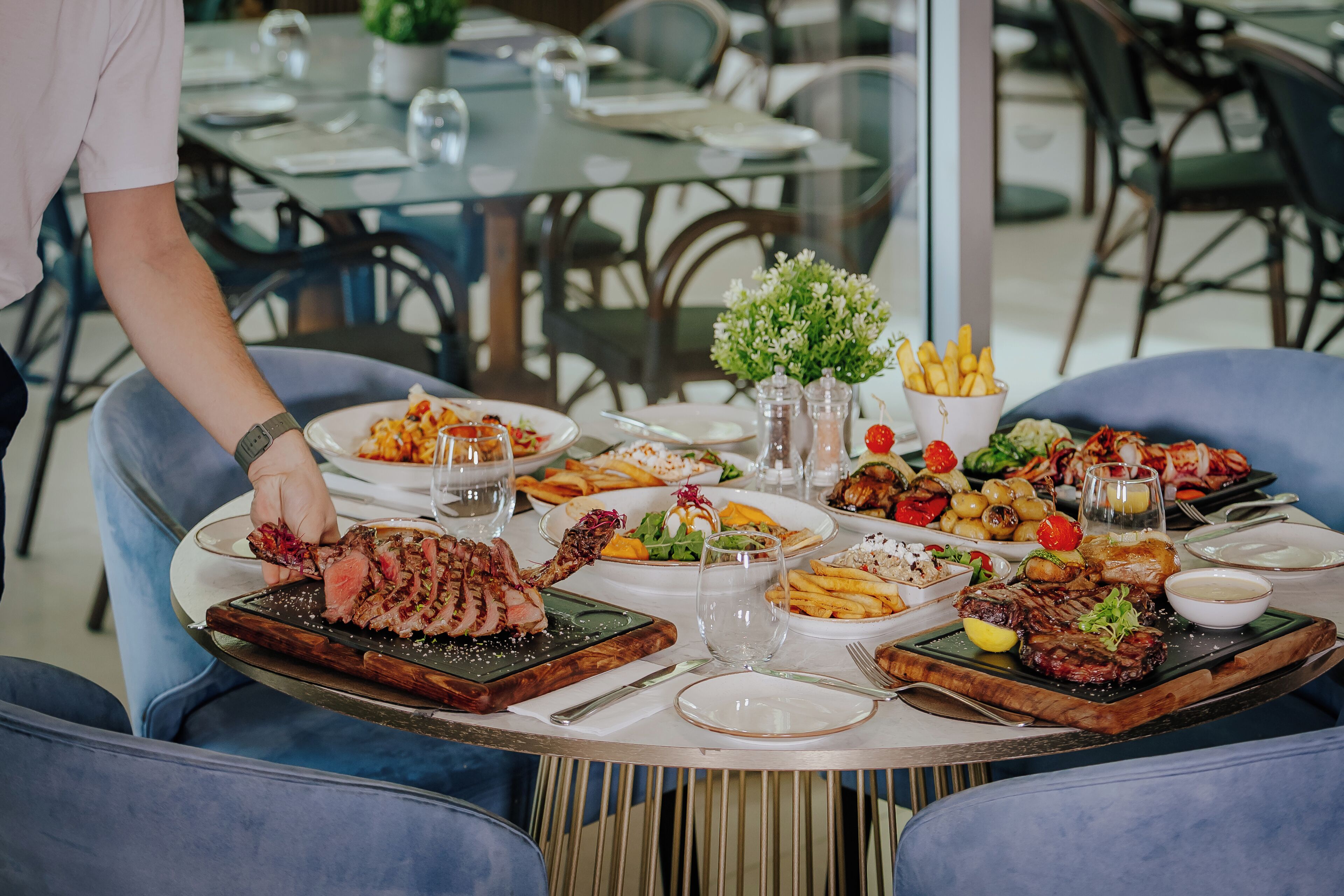 Une table à manger avec différents plats, notamment du steak et des légumes, et une personne qui sert les plats.