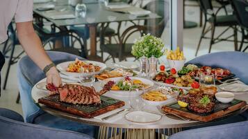 Une table à manger avec différents plats, notamment du steak et des légumes, et une personne qui sert les plats.
