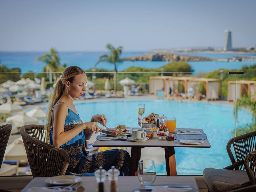 A dining area with a table set for two, overlooking a pool and a view of the ocean and a distant tower.