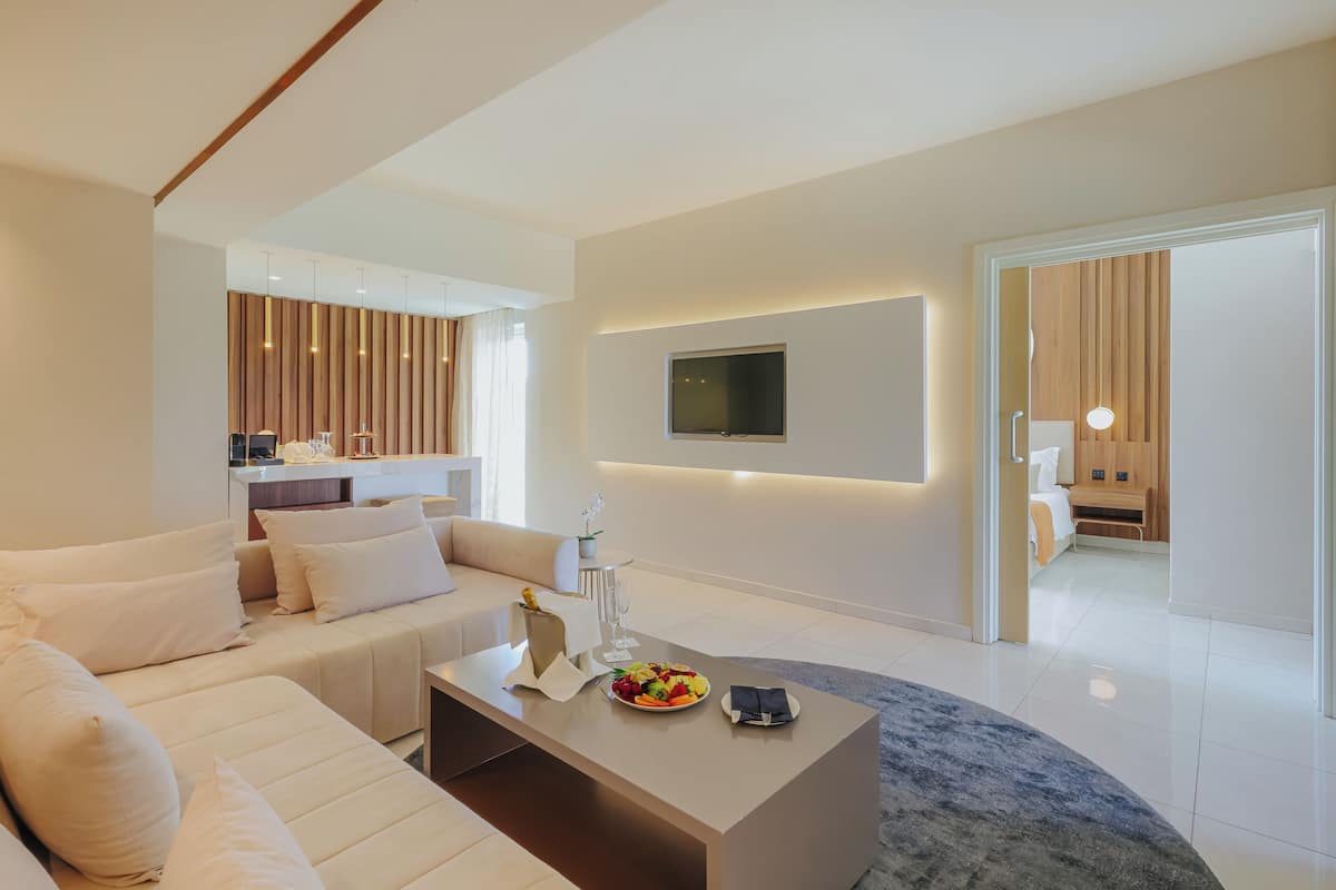 A modern living room with a sofa, coffee table, and TV. There is a kitchen area with wooden paneling and a dining table.