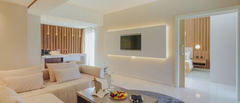 Una sala de estar moderna con sofá, mesa de centro y televisor. Se observa una zona de cocina con paneles de madera y una mesa de comedor.
