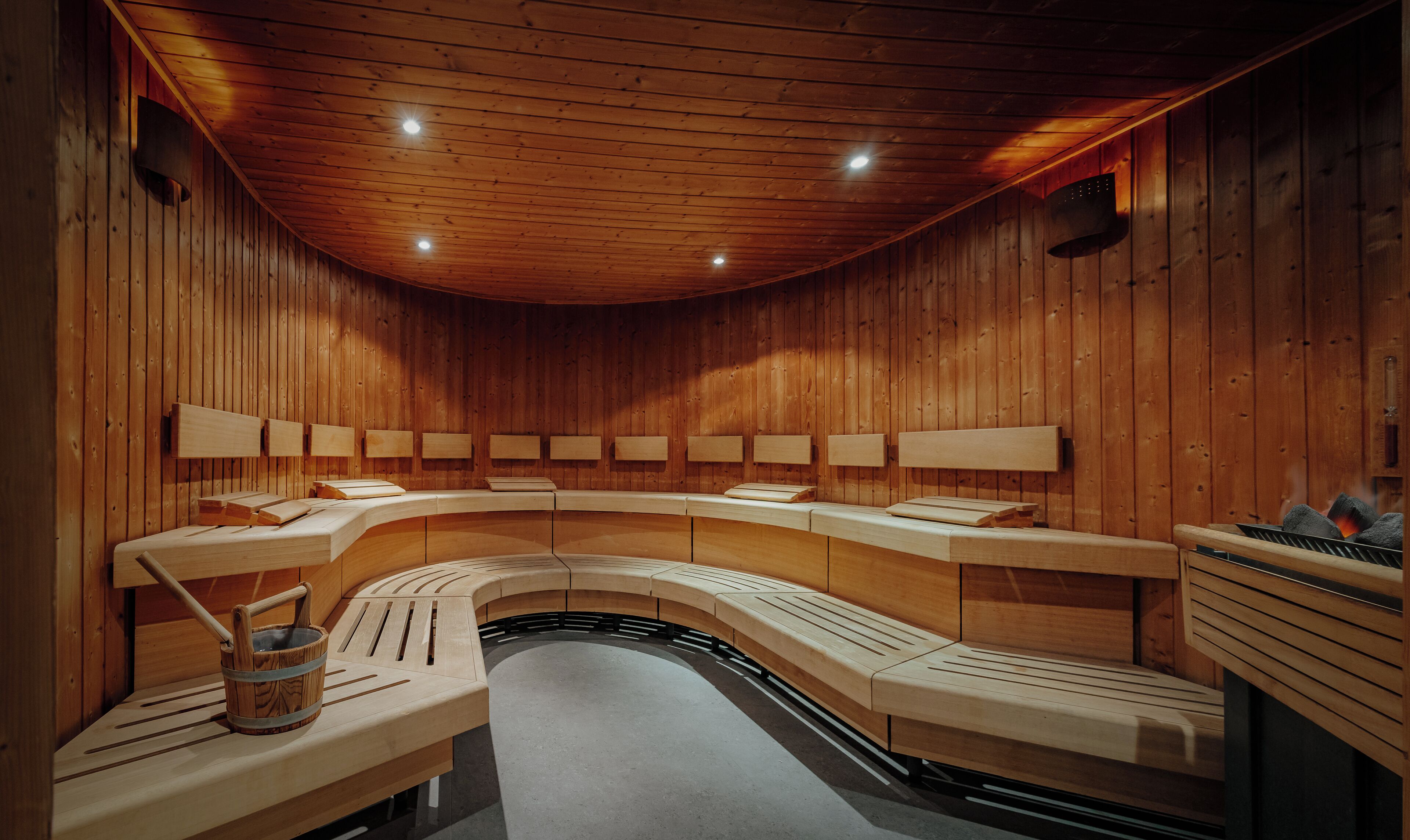 A sauna with wooden benches, benches with towels, and a wooden bucket.