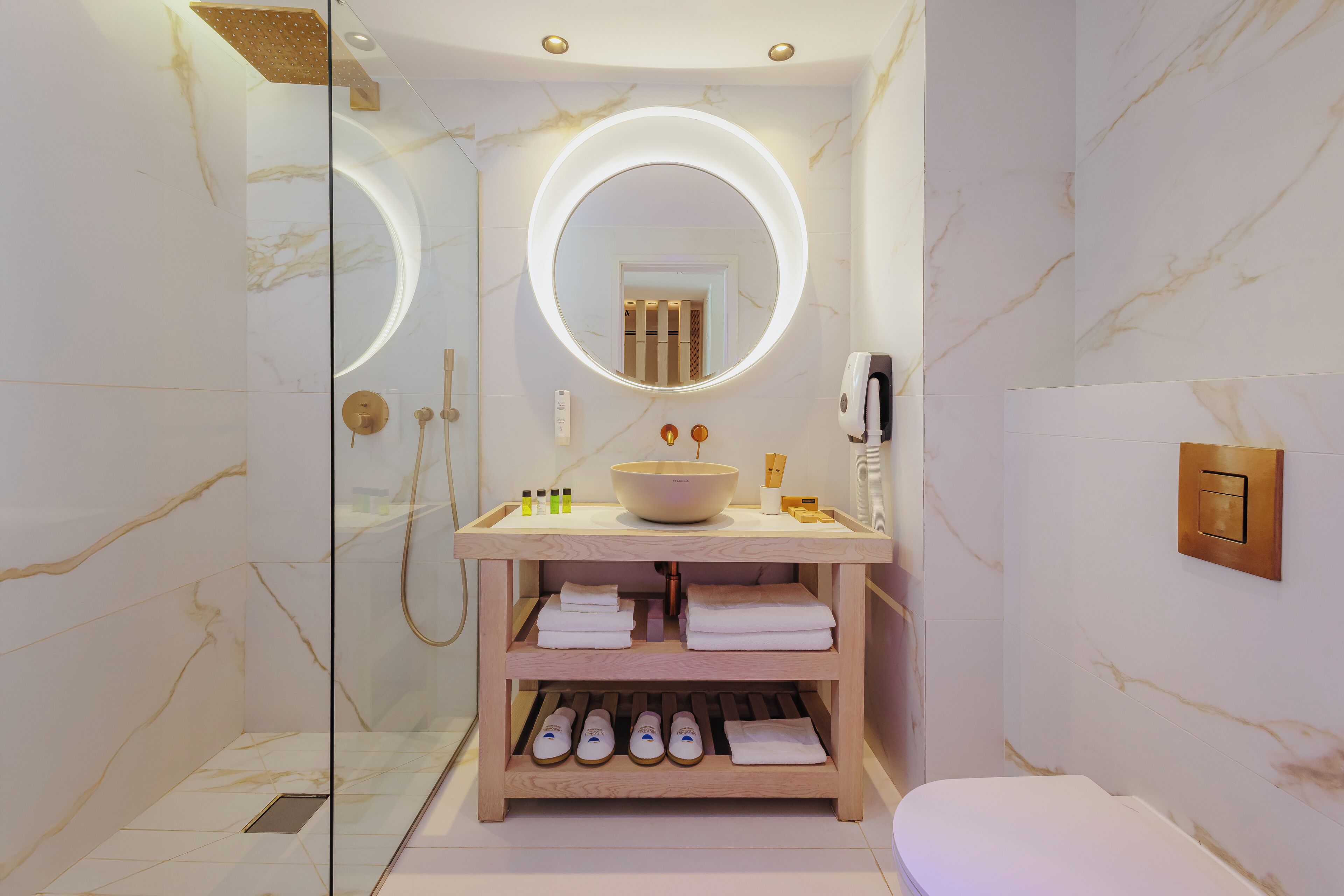 Une salle de bain moderne avec une douche à parois de verre, un grand miroir rond avec éclairage intégré, un meuble-lavabo en bois avec un vasque et des toilettes.