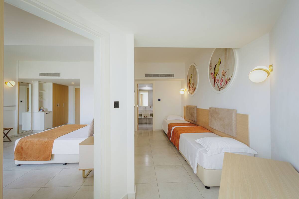 A hotel room with two beds, a bathroom, and a hallway leading to another room.