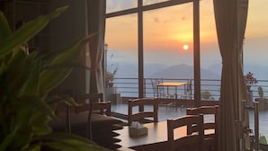Ein Zimmer mit großen Fenstern und einem weiten Blick auf Berge und einen Sonnenuntergang.